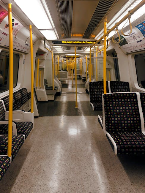 A close-up view of the side of a London Underground train, featuring red and cream-colored exterior panels with rectangular, tinted windows framed in grey. The train is stationary on the tracks, with